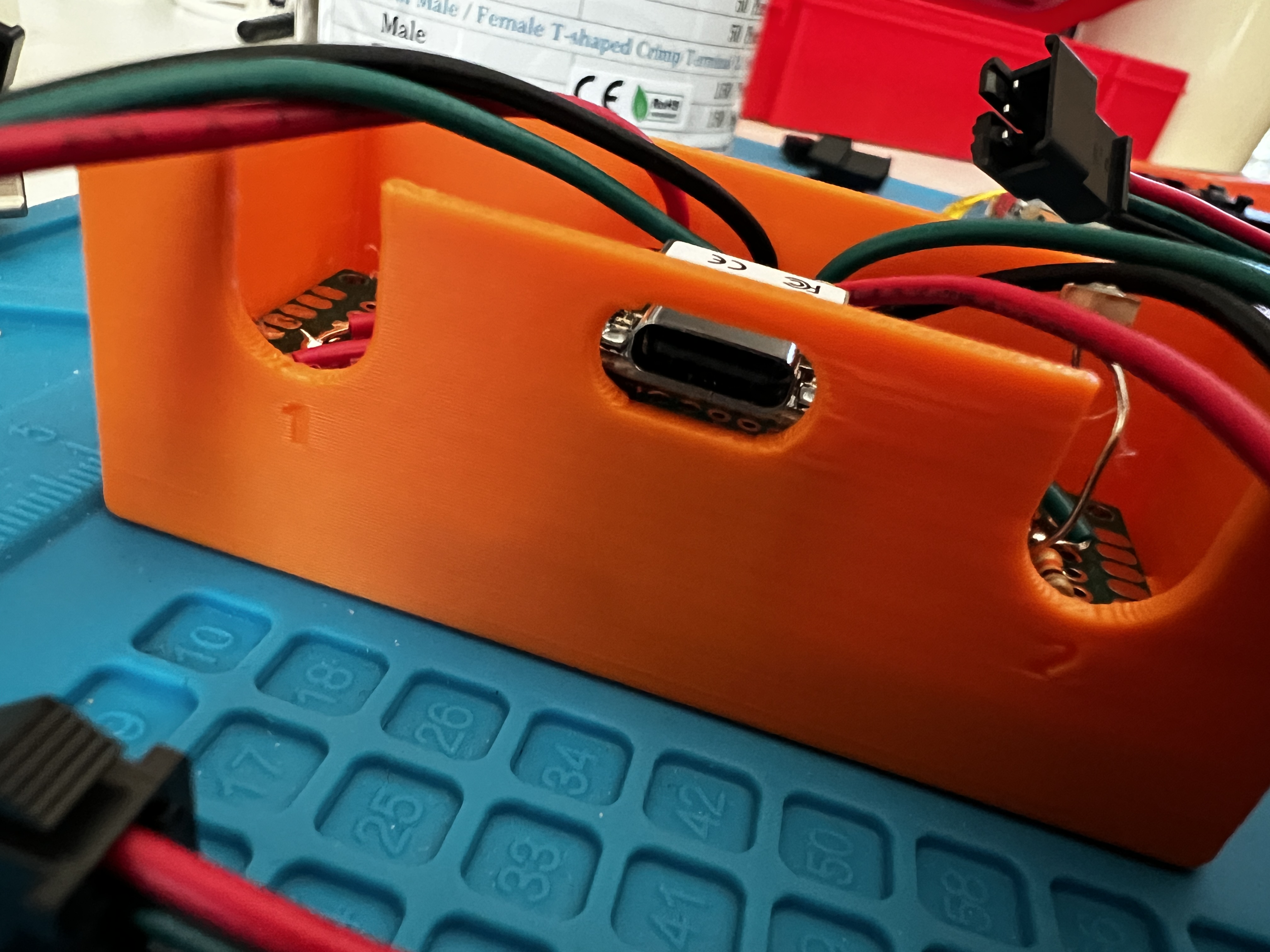 The lantern's orange 3D-printed enclosure on a blue work mat, USB-C port on the near end, LED power and data wires running out to JST connectors.